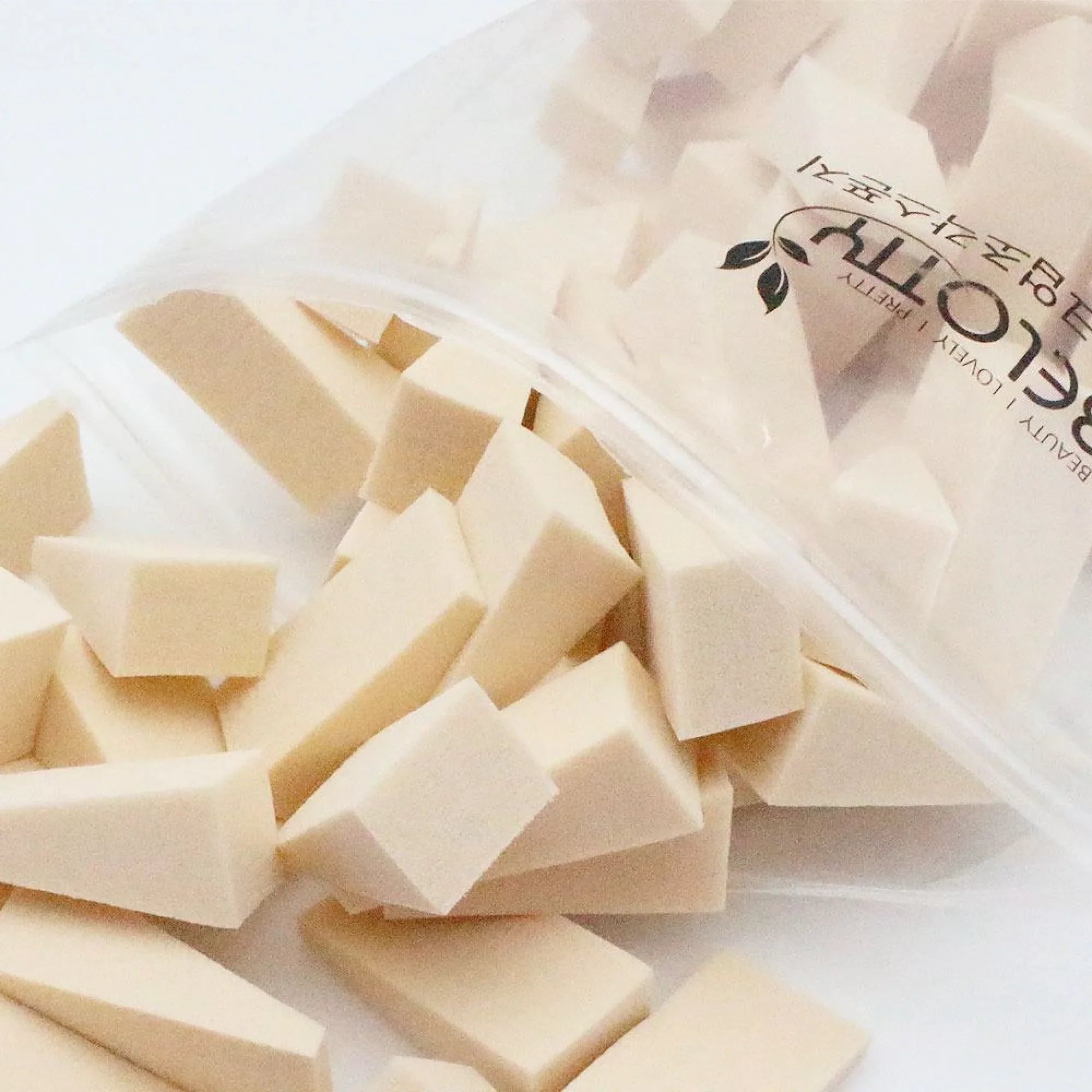Beige sponges in a clear plastic bag with branding on a white background